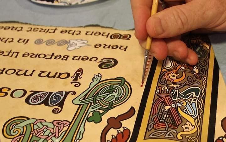 A hand with a paint brush creating a Celtic illumination artwork.